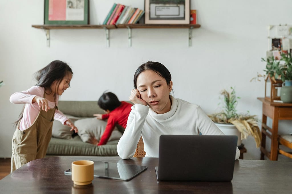 A tired mother looking for picture-perfect image on her laptop for instagram while children play in the background.