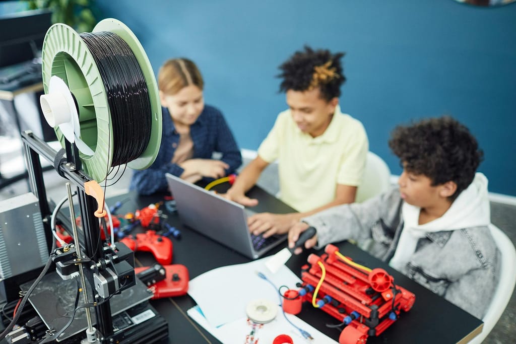 Children collaborating on a STEM project with a 3D printer and laptop in an educational setting.