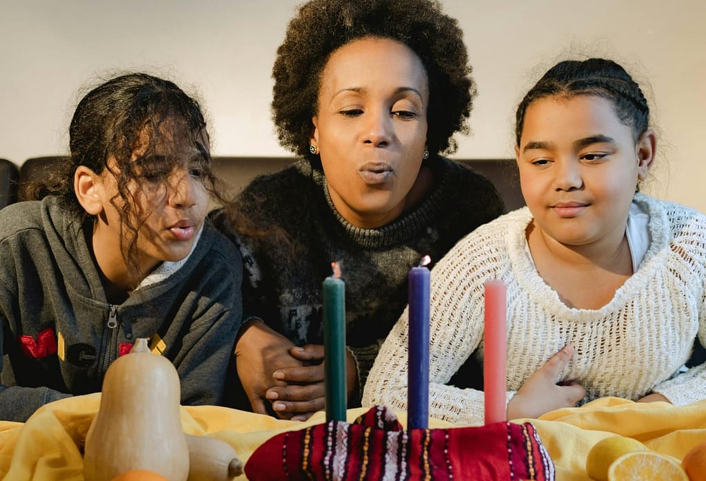 A mother and daughters celebrate Kwanzaa with candles, symbolizing unity and joy.